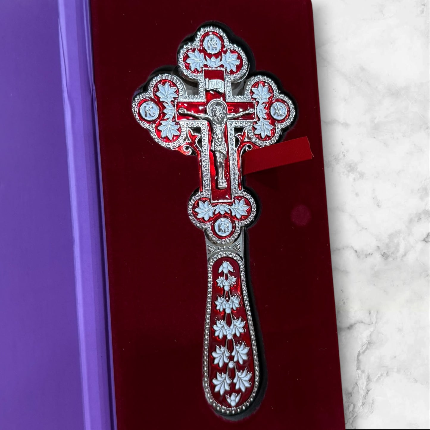 Double-sided red and white enamel blessing cross with metal crucifix displayed inside a premium gift box.