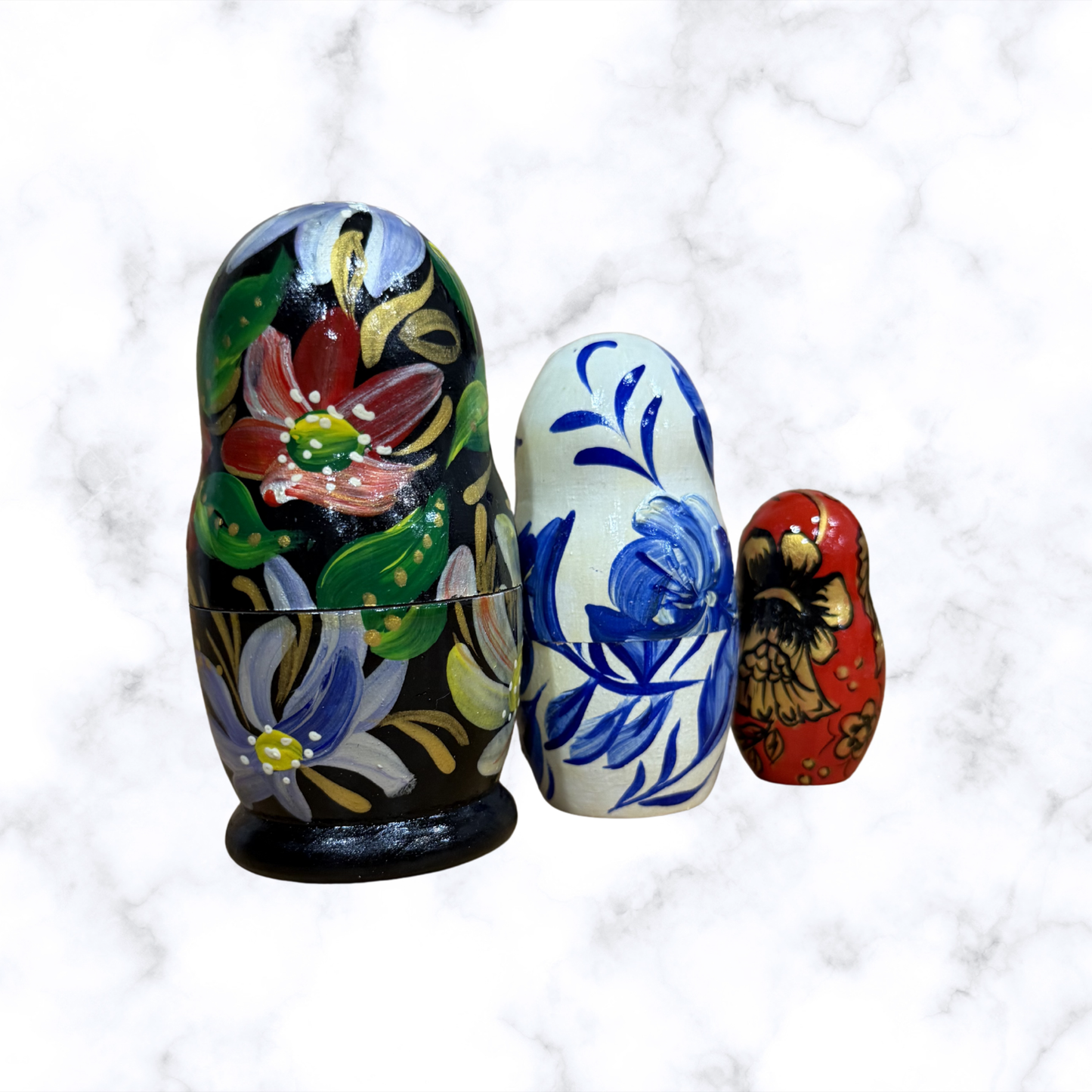 Three hand-painted Russian nesting dolls with colorful floral designs displayed together, featuring a traditional Matryoshka doll set.