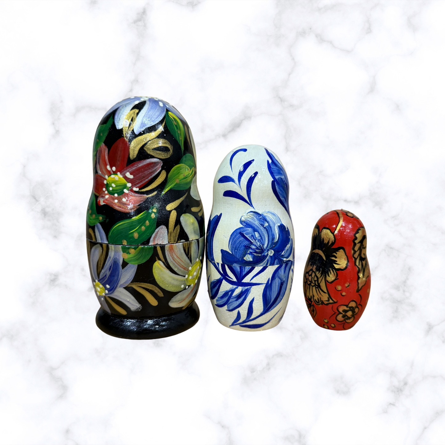 Three hand-painted Russian nesting dolls with colorful floral designs displayed together, featuring a traditional Matryoshka doll set.