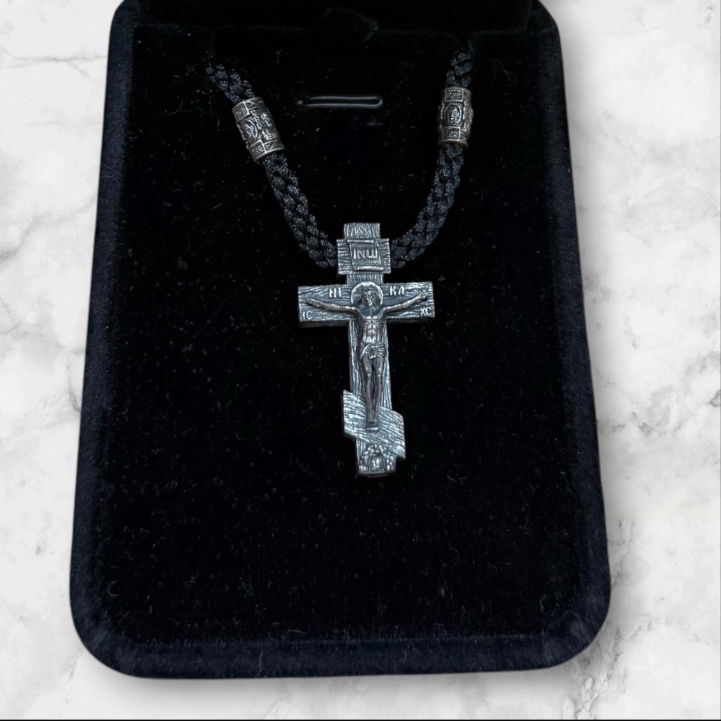 Orthodox crucifix pendant with braided black cord displayed in a gift box