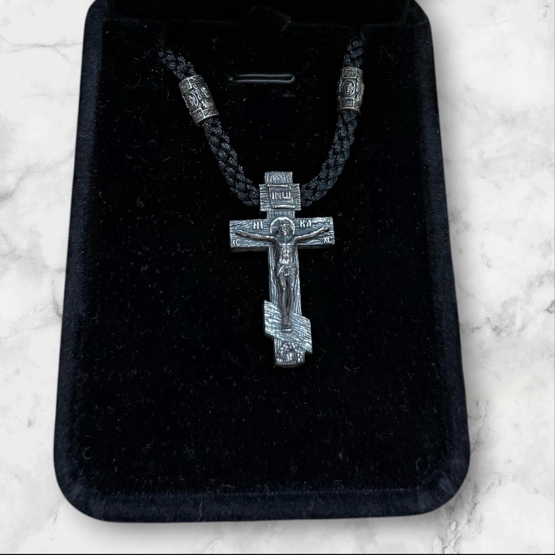 Orthodox crucifix pendant with braided black cord displayed in a gift box