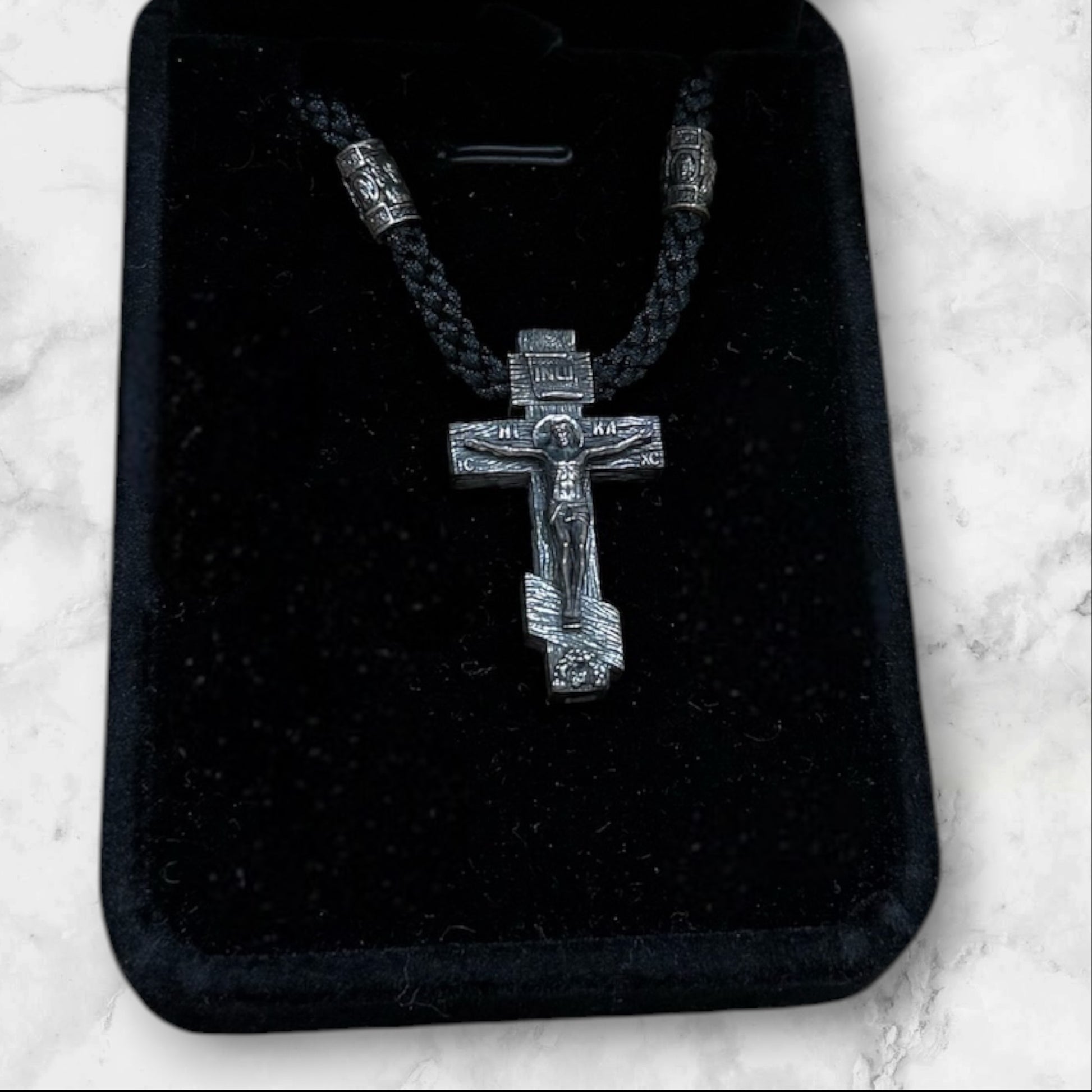 Orthodox crucifix pendant with braided black cord displayed in a gift box